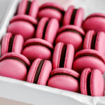Pink macarons filled with dark chocolate in the white and pink box.