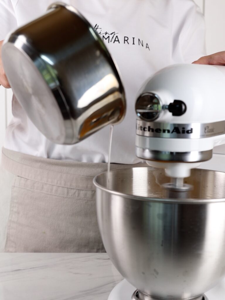 Pouring sugar syrup into the mixing bowl of the stand mixer.