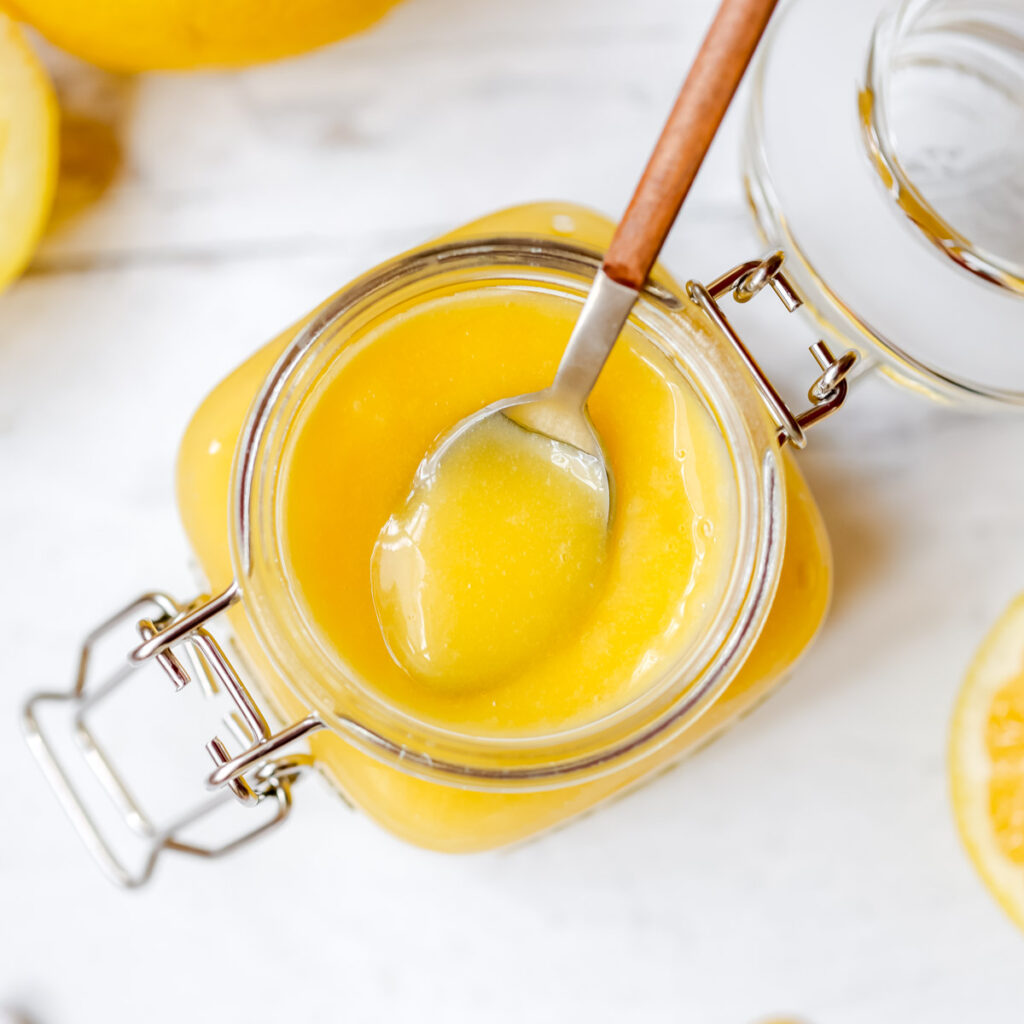 Glass jar with lemon curd and a spoon on the table.