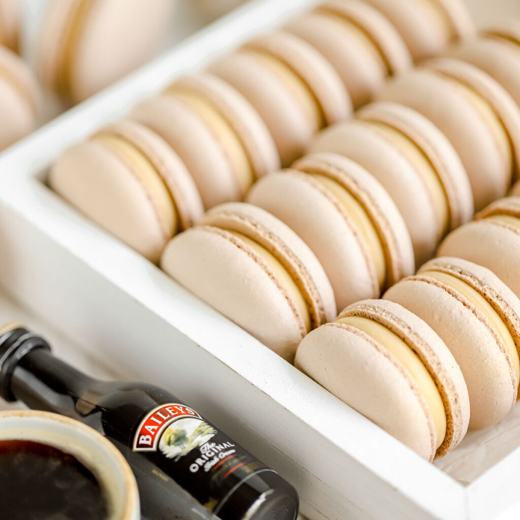 Macarons in the white box with a cup of coffee and a bottle of Baileys.