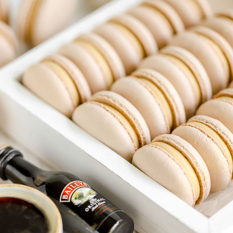 Macarons in the white box with a cup of coffee and a bottle of Baileys.