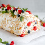 Meringue roulade on the table with fresh berries on the top.
