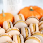 Orange macarons on the table with pumpkin in the background.