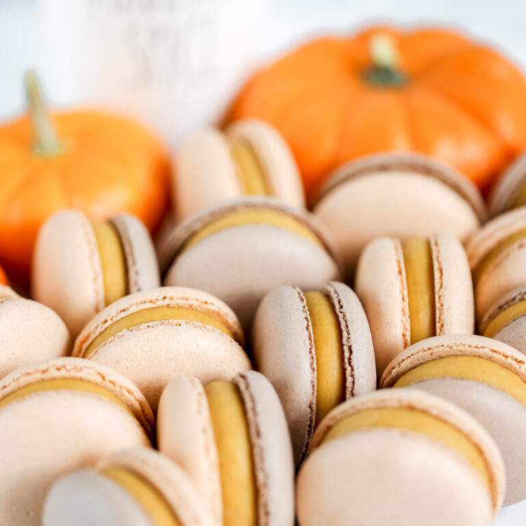 Orange macarons on the table with pumpkin in the background.