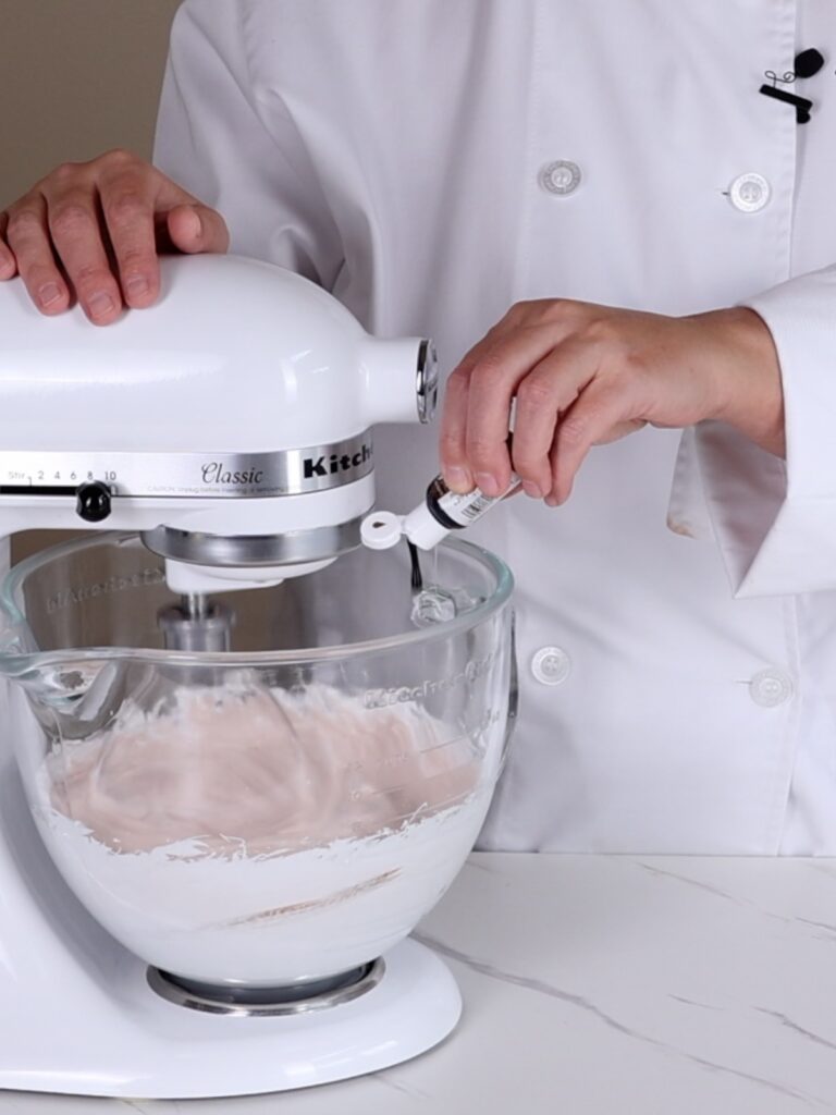 Hand adding brown food coloring into the mixing bowl.