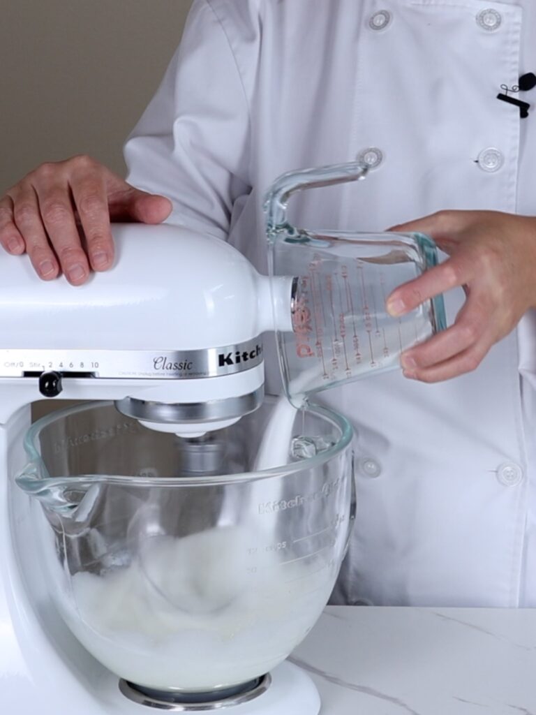 Hand pouring sugar into the mixing bowl.