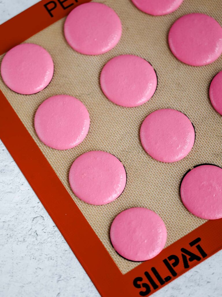 Pink macarons are pipped on the baking mat. 