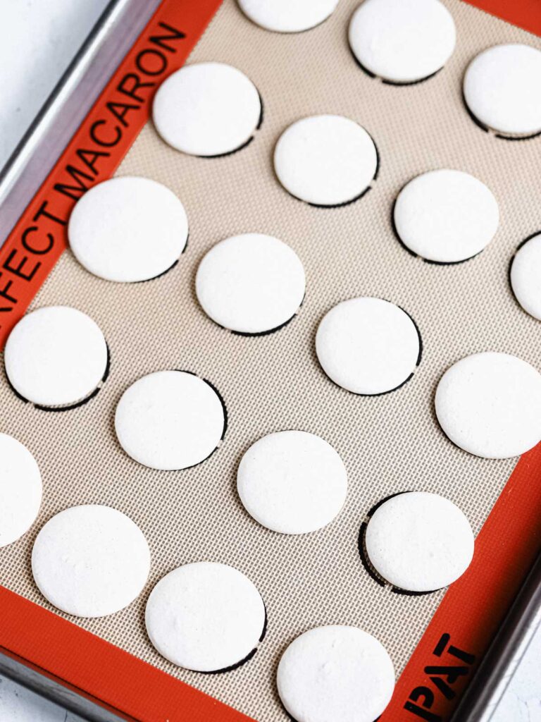 White macaron shells on the baking mat. 