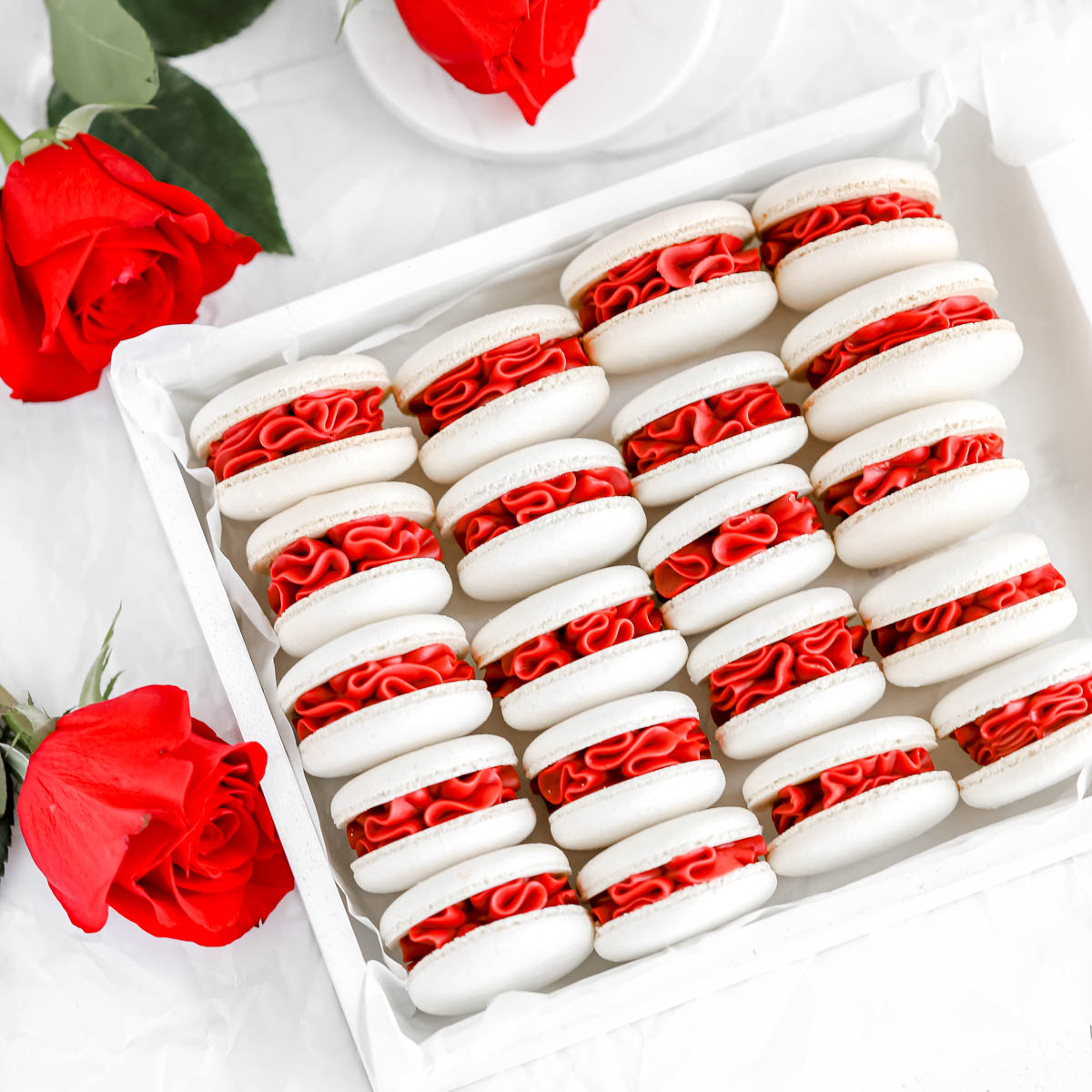 White macaron shells filled with red velvet ganache in the box.
