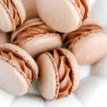 Brown macarons filled with chocolate cheesecake filling on the plate.