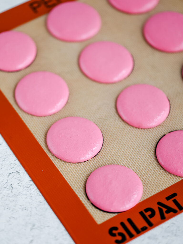 Pink macarons piped on the baking mat. 