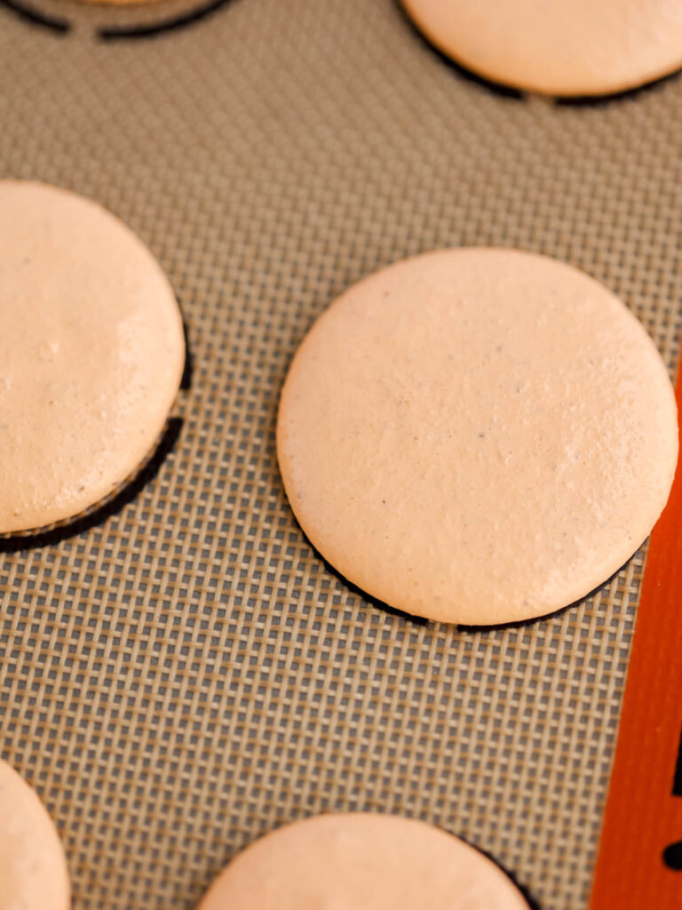 Orange macarons on the baking mat. 