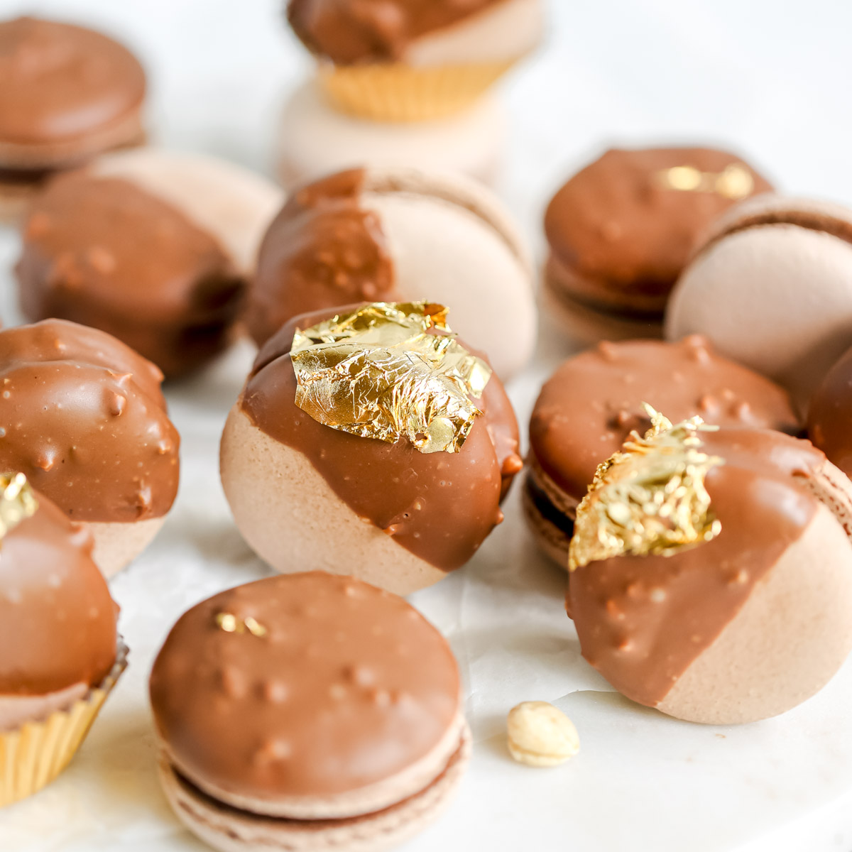 Chocolate macarons covered in chocolate glaze and decorated with gold leaves.