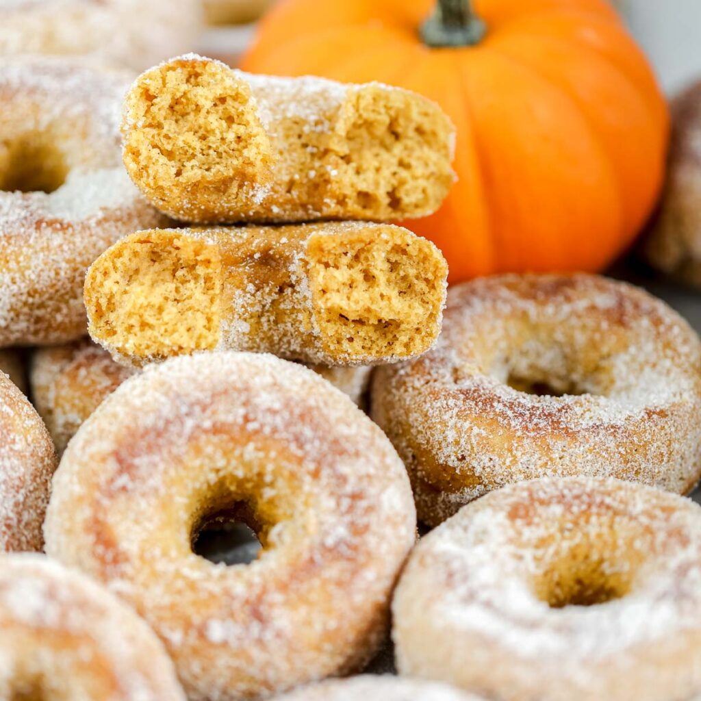 Pumpkin donuts with the orange pumpkin in the background.