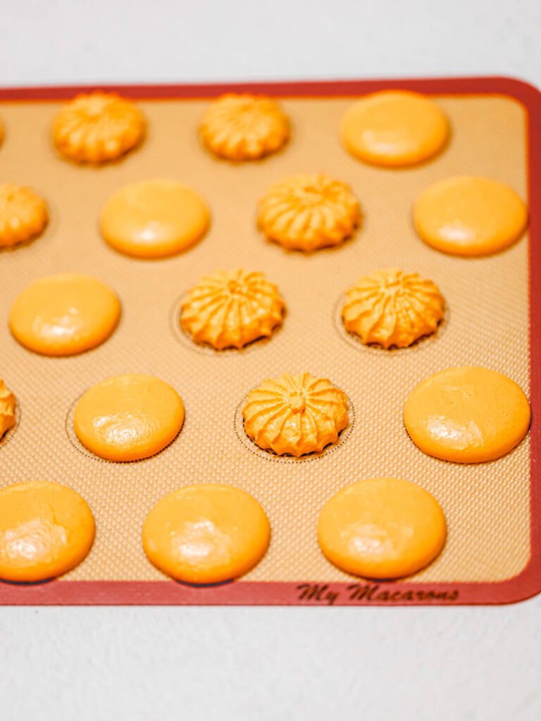 Orange macaron shells piped on the baking mat. 