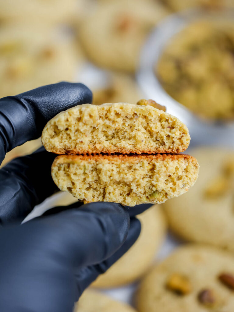 Hand holding a pistachio cookie cut in half. 