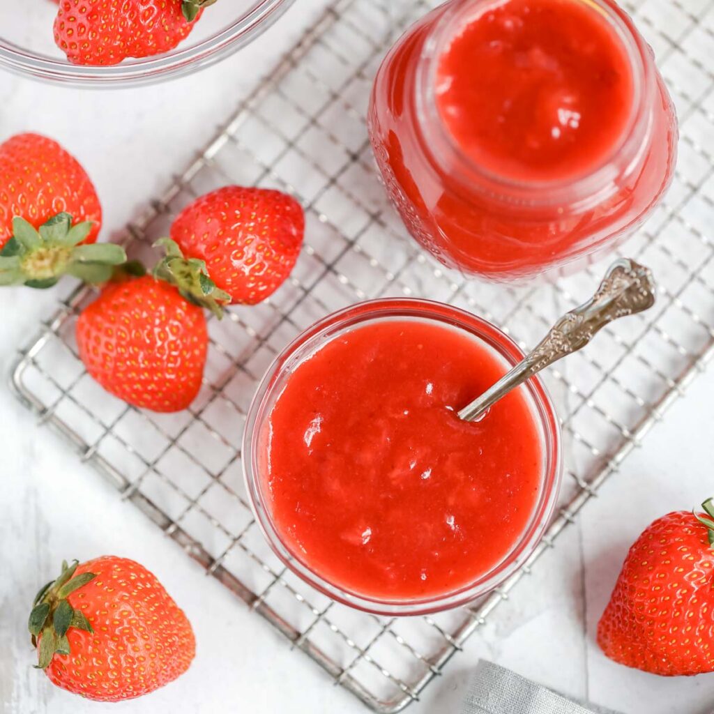 Strawberry sauce in the glass jar and fresh strawberries in the small glass bowl on the side.