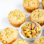 Pistachio muffins with a bowl of pistachios on the table.