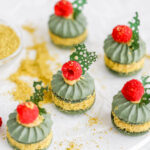 Green round cookies with pistachio ganache and fresh raspberry on the top.