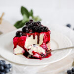 A piece of cheesecake on the plate, topped with blueberry sauce.