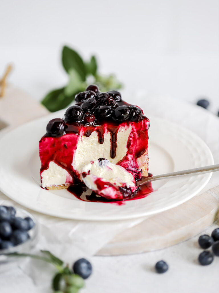 A piece of cheesecake on the plate, topped with blueberry sauce.