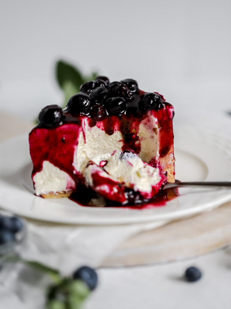 A piece of cheesecake on the plate, topped with blueberry sauce.