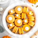 Orange macarons are decorated with meringue cookies on top.
