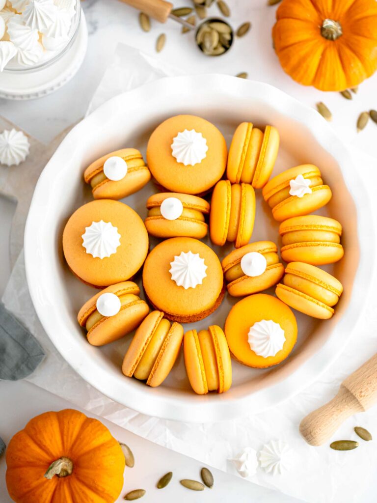 Orange macarons are decorated with meringue cookies on top.