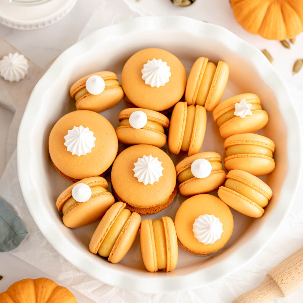 Orange macarons decorated with meringue cookies on top.