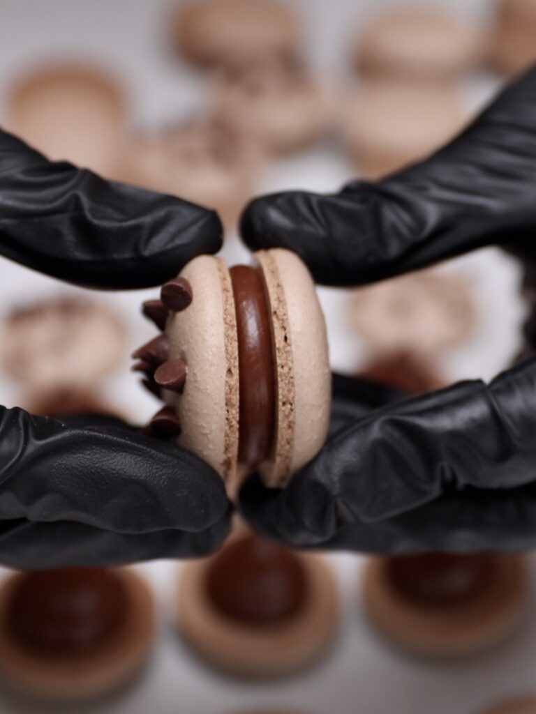 Hands are sandwiching a macaron. 