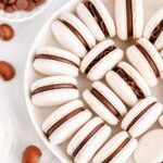 White macarons filled with chocolate ganache on a white plate.