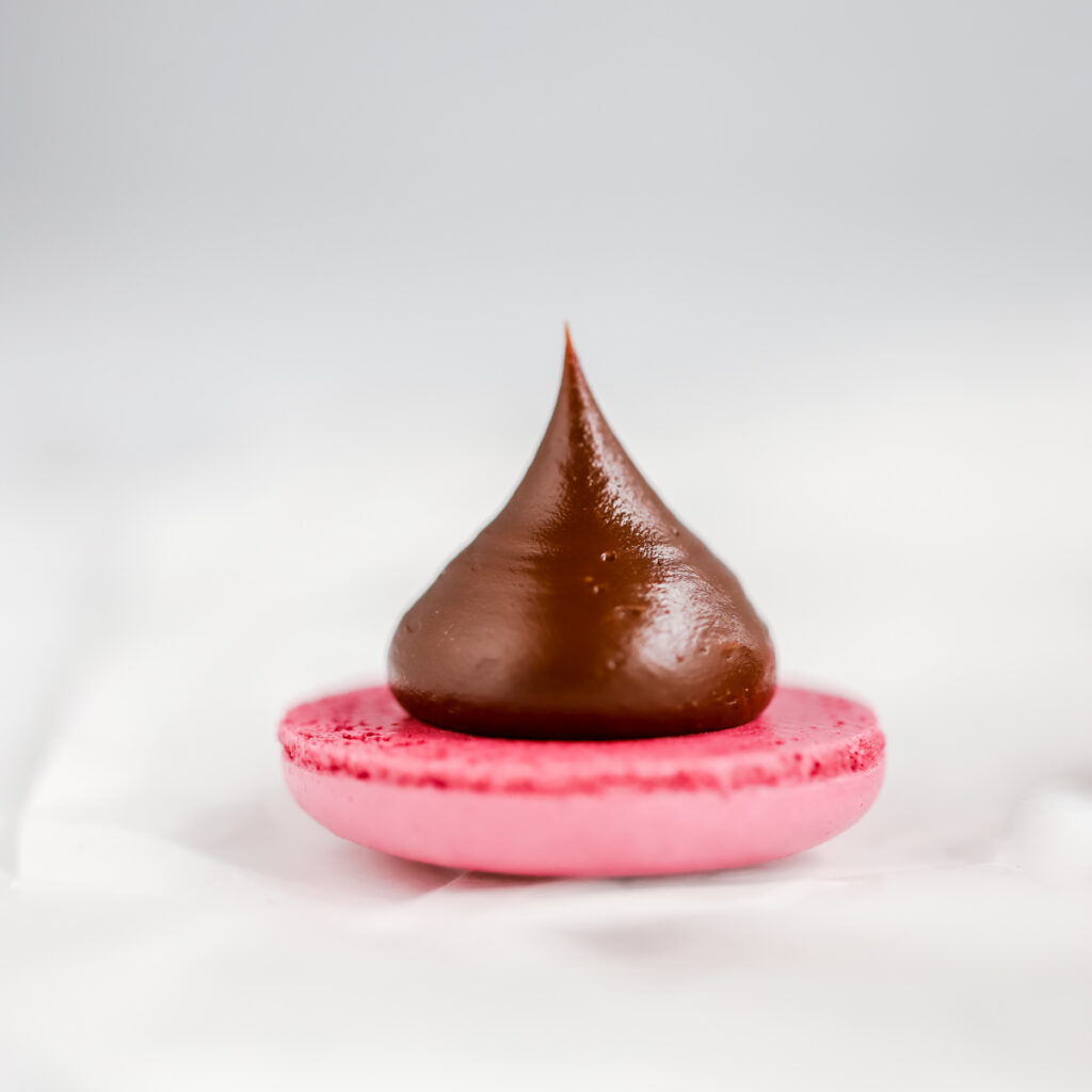 Dark chocolate ganache piped on pink macaron shell.