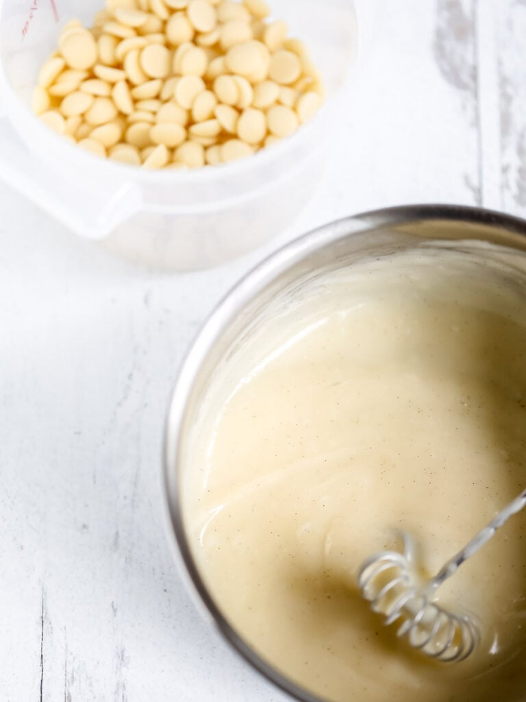 Pastry cream in the saucepan and white chocolate in the plastic cup.