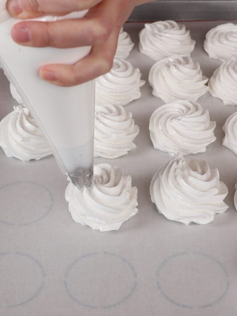 Hand is piping Apple Zephyr on the parchment paper.