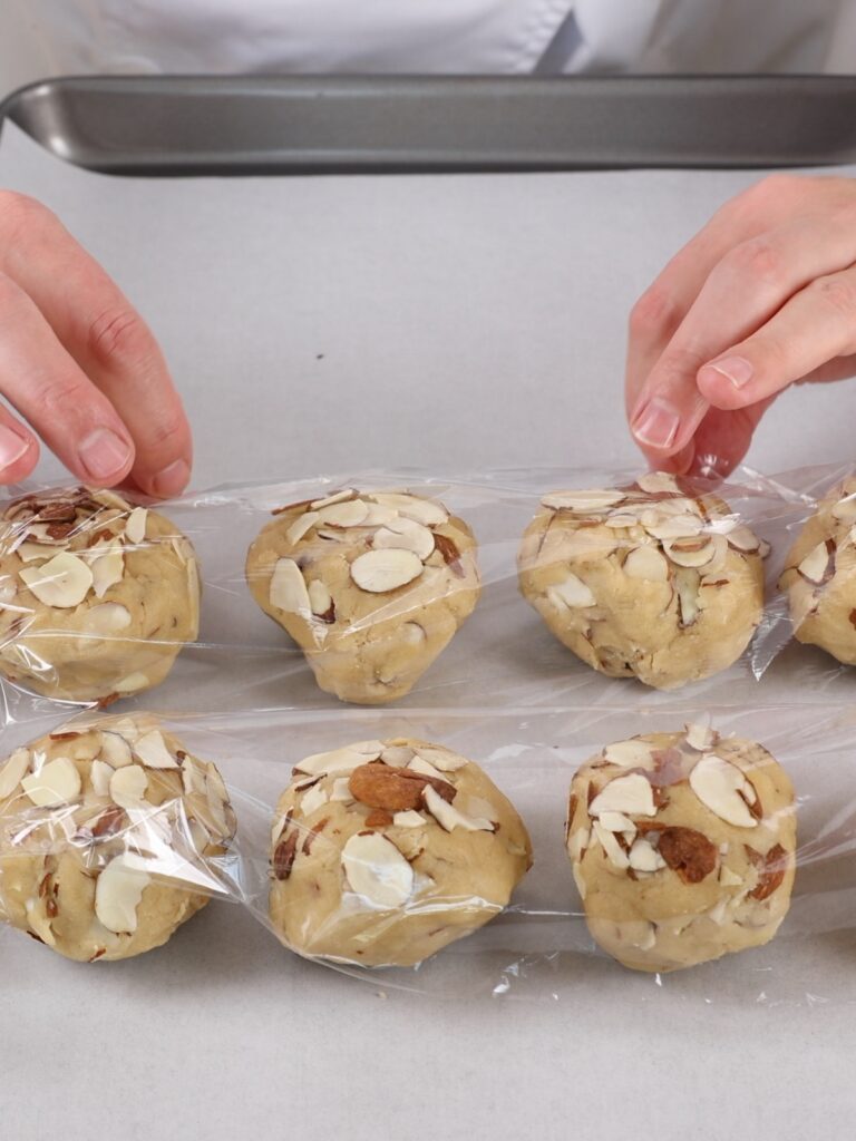 Hands are covering cookie balls with plastic wrap. 
