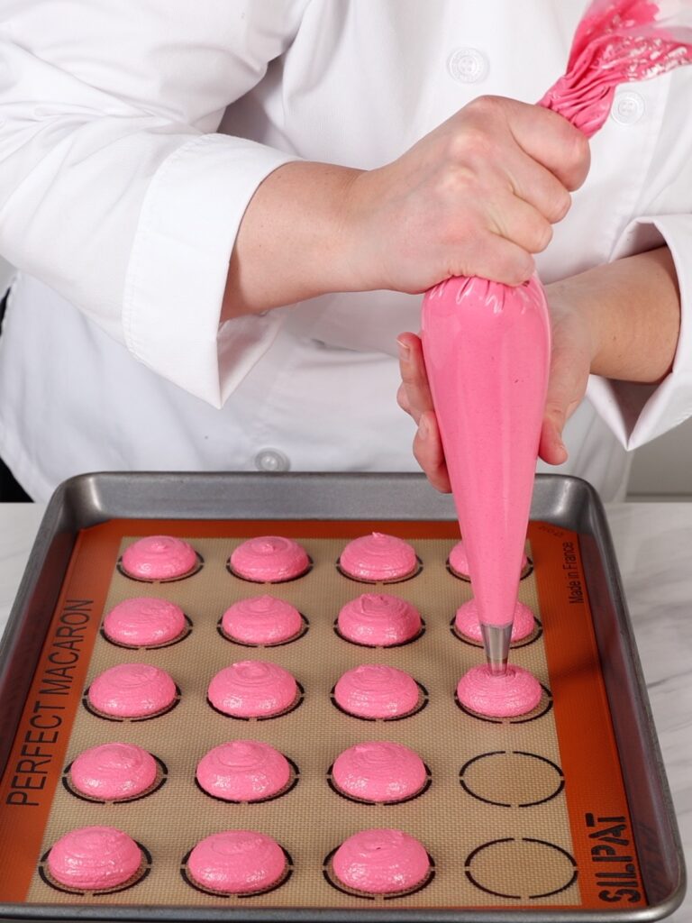 Piping pink macaron shells on the baking mat.