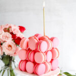 A macaron cube cake on the table with pink flowers in the vase.