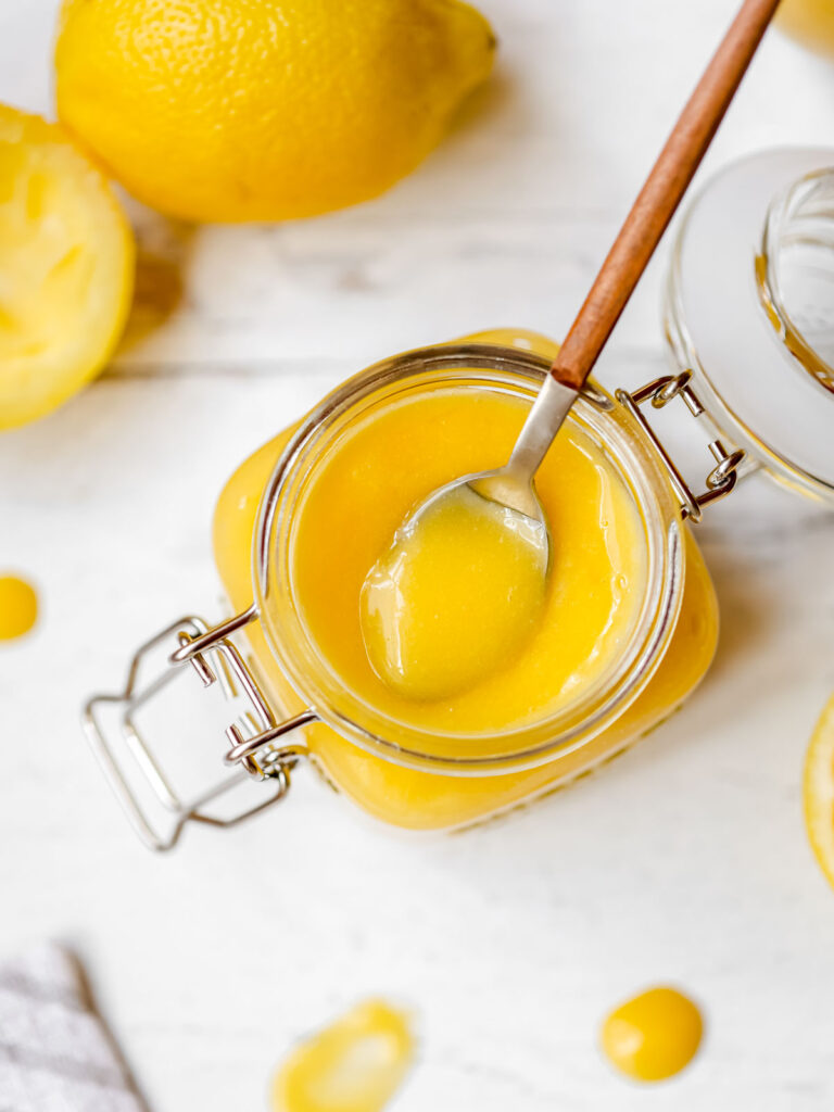 Lemon curd in the glass jar with the spoon. 