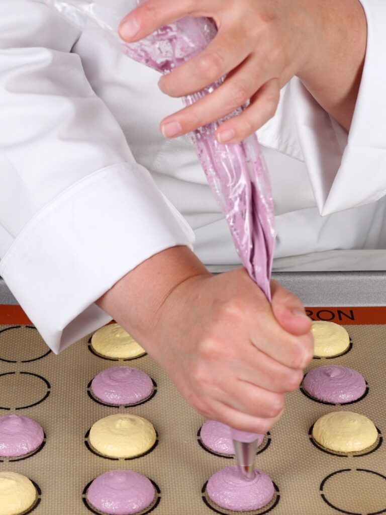 Piping macaron shells on the baking mat. 