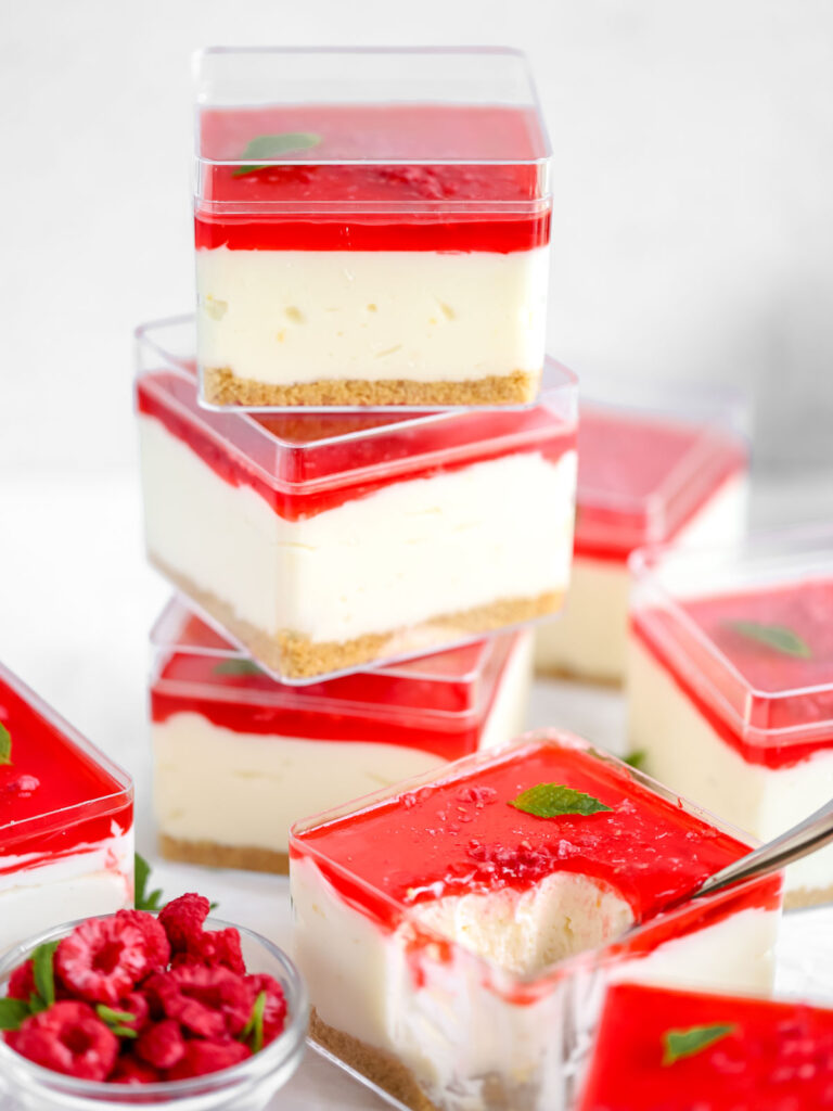 Cheesecake in a cube container with raspberry jello on the top.