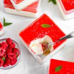 Cheesecake in a cube container with raspberry jello on the top.