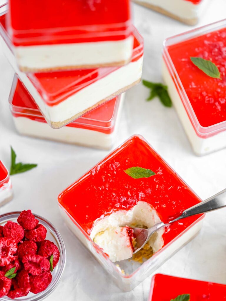 Cheesecake in a cube container with raspberry jello on the top.