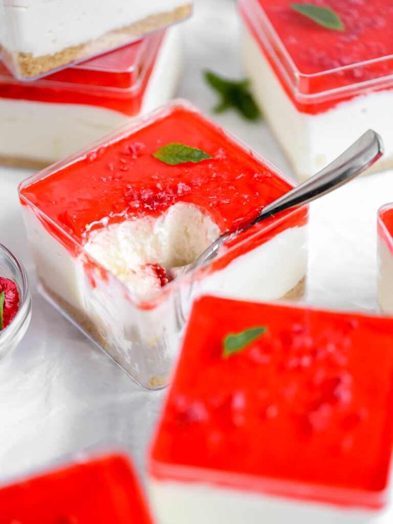 Cheesecake in a cube container with raspberry jello on the top.