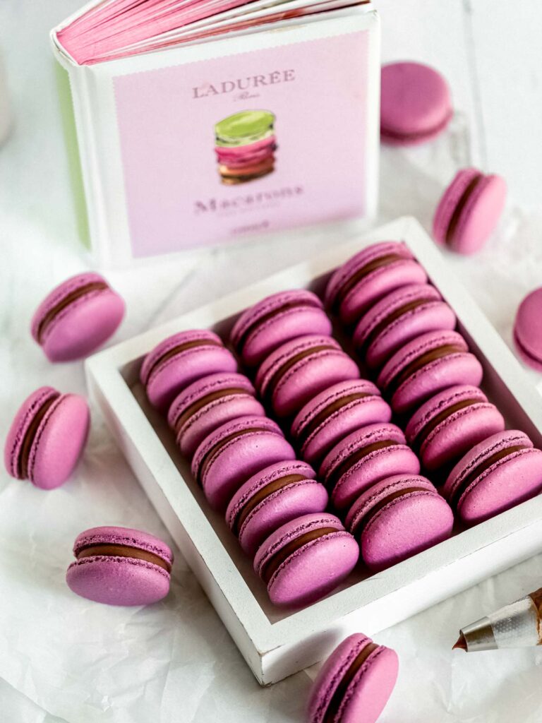 Purple macarons in the box with the Ladurée book in the background. 
