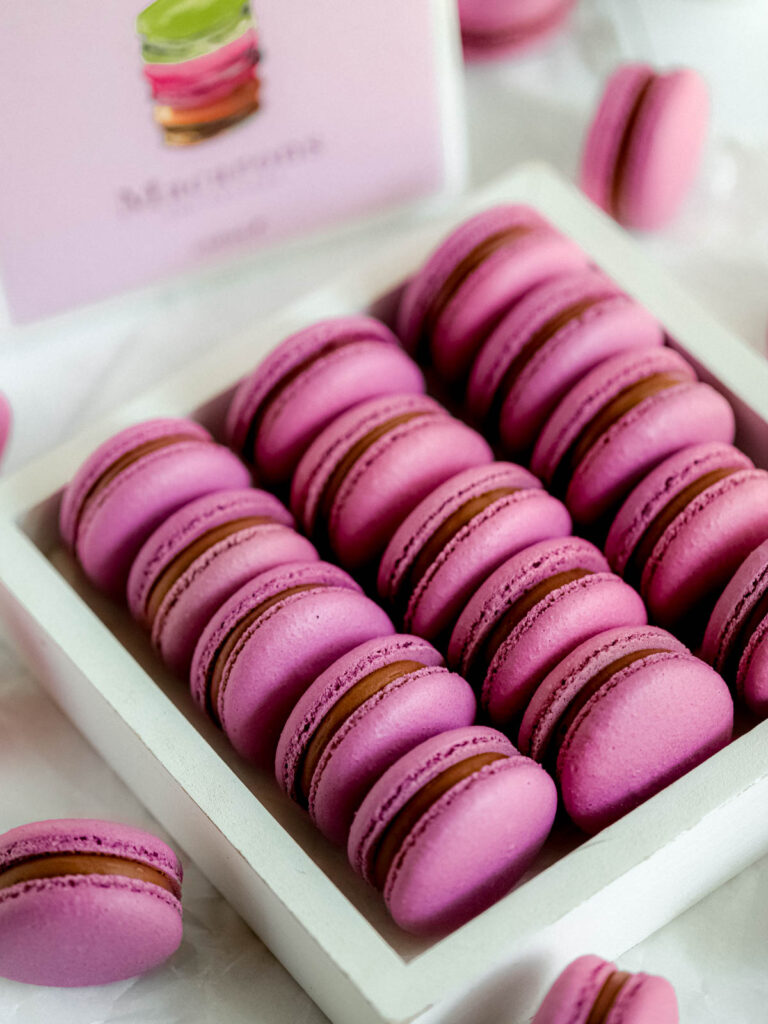 Purple macarons in the box with the Ladurée book in the background.