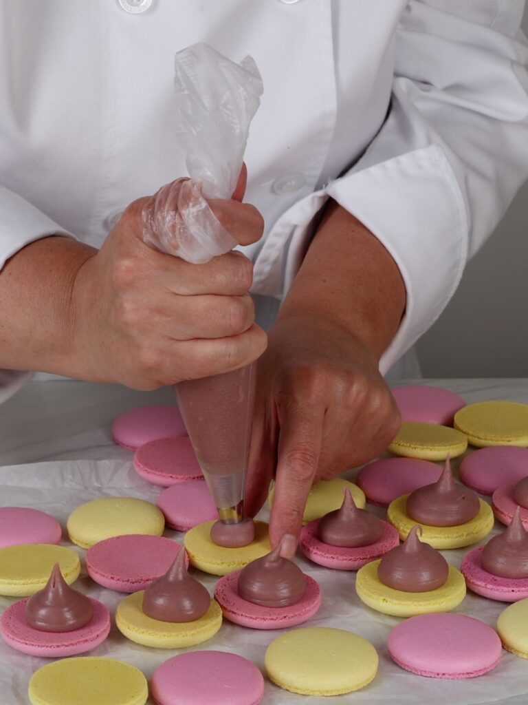 Piping raspberry ganache on flat side of macaron. 
