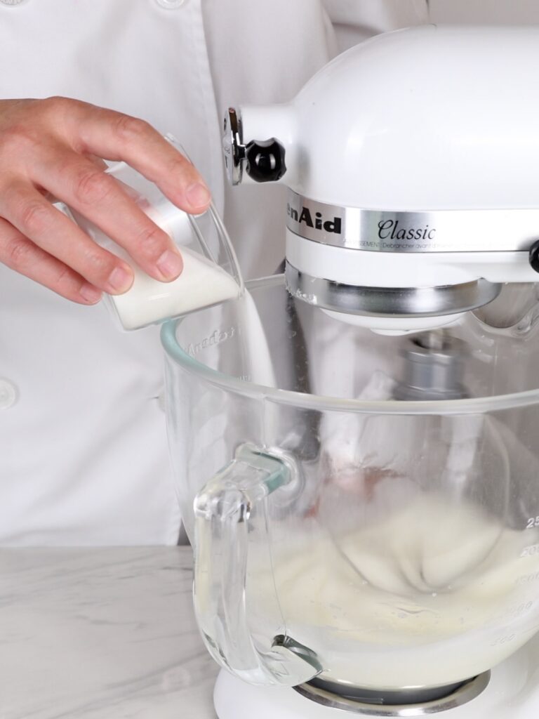 Adding sugar to egg whites in the mixing bowl. 