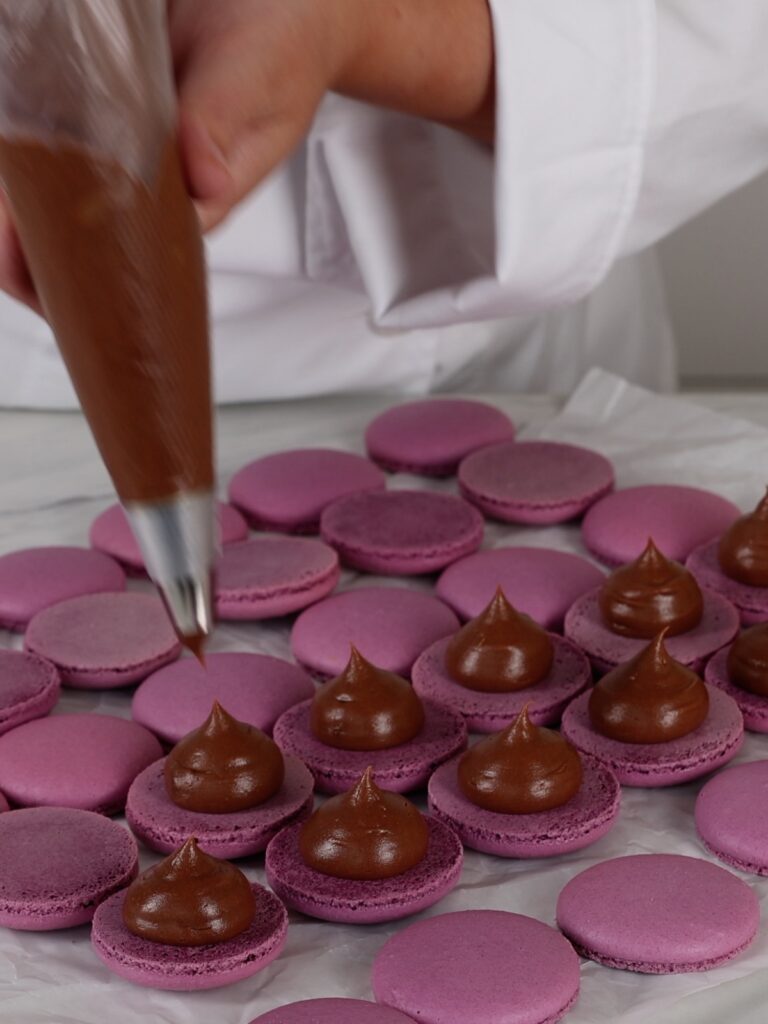 Piping ganache on the purple macaron shells. 