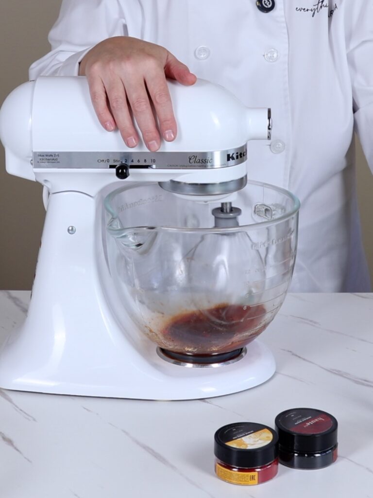 Mixing bowl of a stand mixer with egg whites and food coloring.