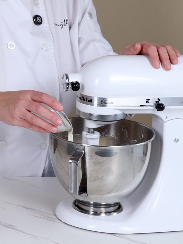The hand is adding heavy cream into the mixing bowl.